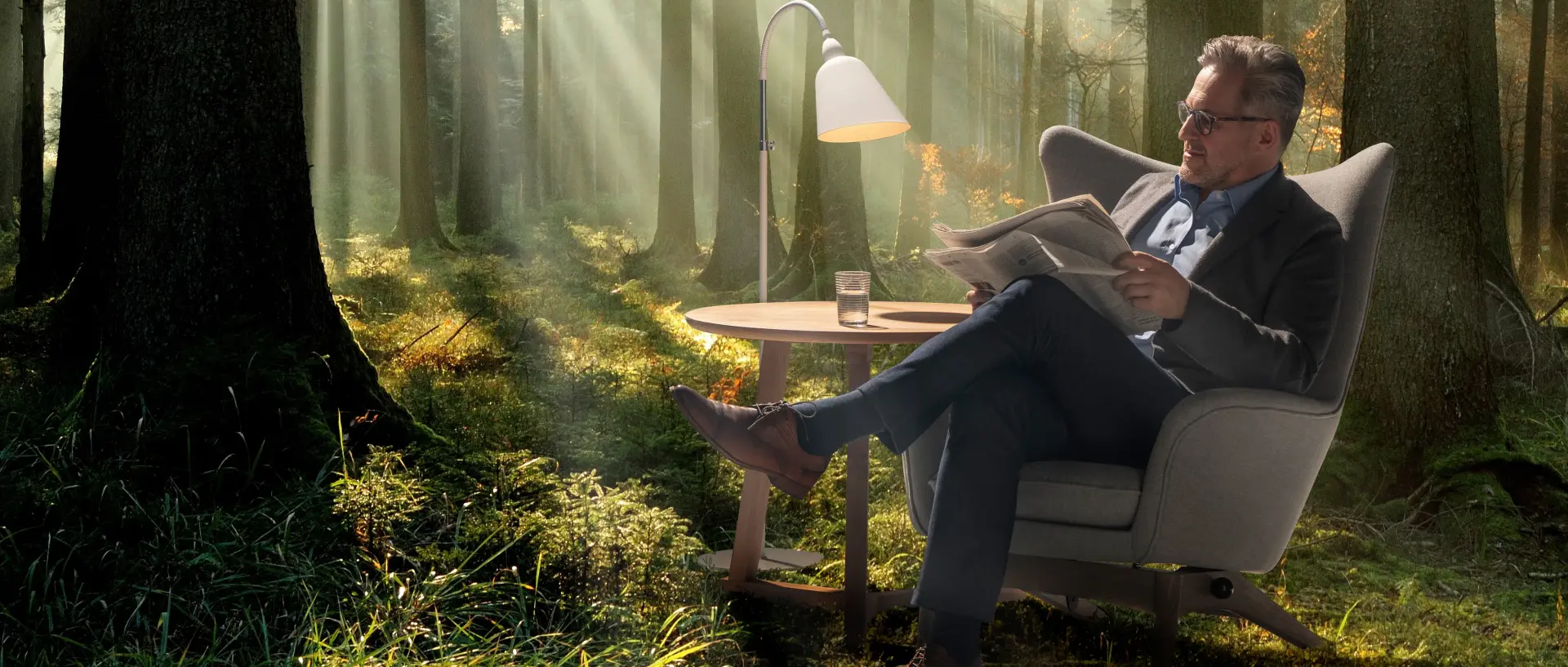 Mann sitzt in einem Sessel im Wald und liest ganz entspannt Zeitung